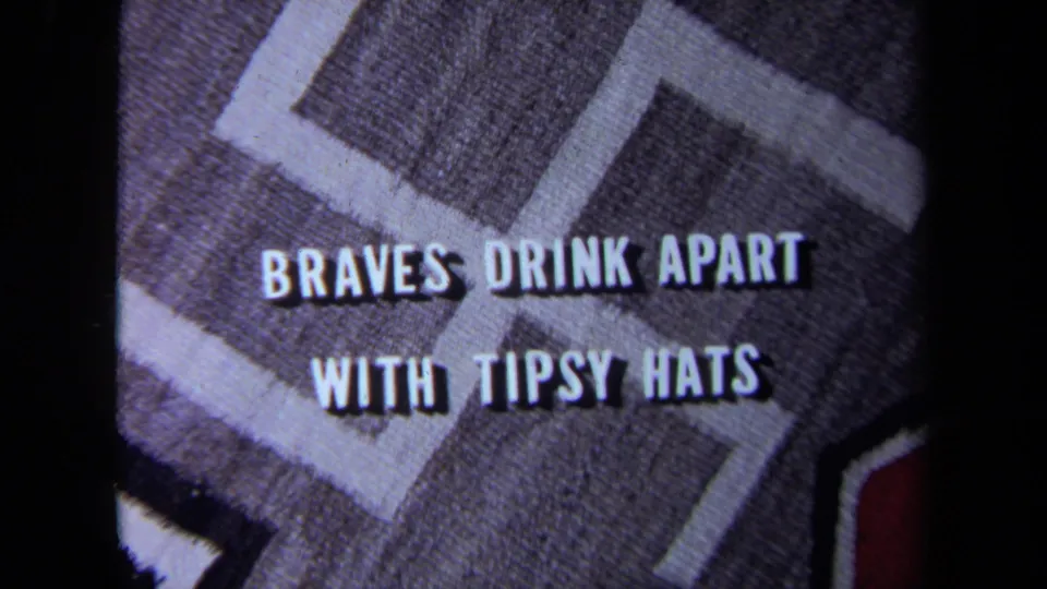 1971 home-movie title card with white lettering over patterned fabric, reading “BRAVES DRINK APART WITH TIPSY HATS.”