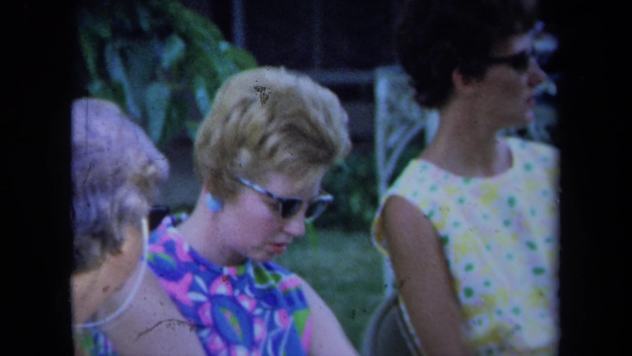 Adult women in sunglasses sit outdoors on lawn chairs beside leafy plants.
