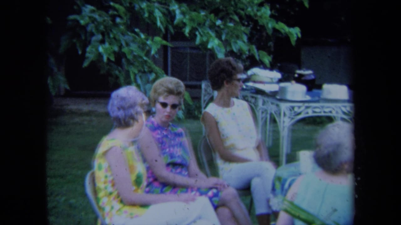 Women seated outdoors on lawn chairs near a white patio table under leafy shade.