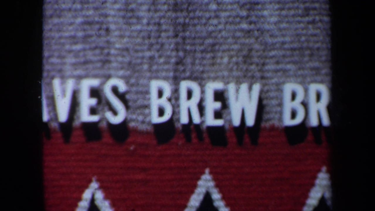 Closer-focused sign detail with white letters, gray texture, red band, and white triangles.