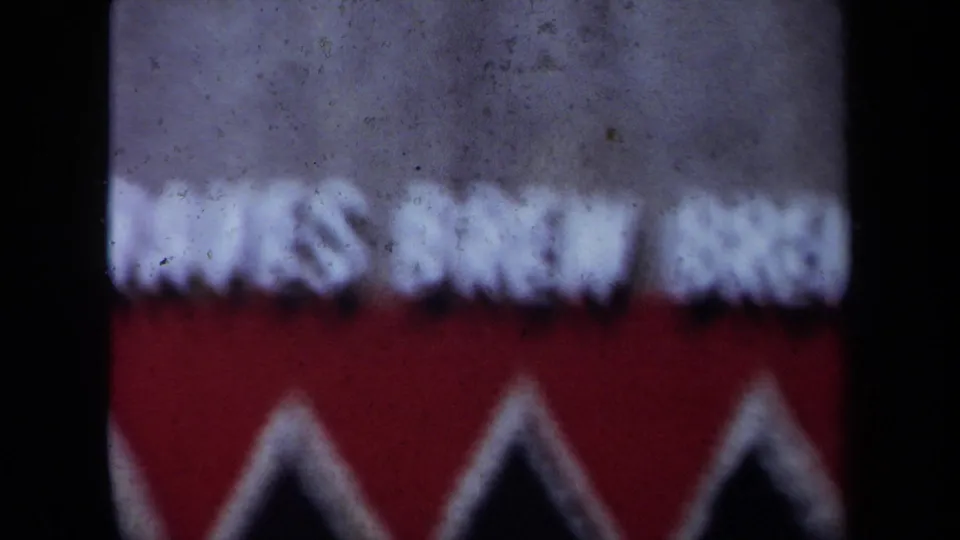 Soft, out-of-focus 8mm frame showing a red and white patterned surface, likely an incidental detail before the gathering view.