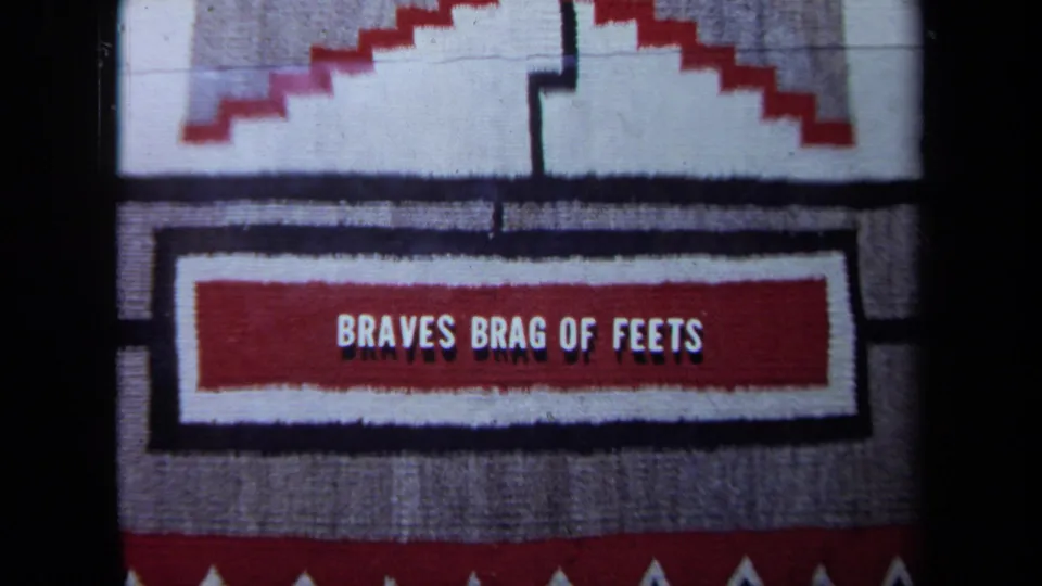 The camera frames the textile more tightly, showing stepped red-and-white motifs and the phrase BRAVES BRAG OF FEETS.