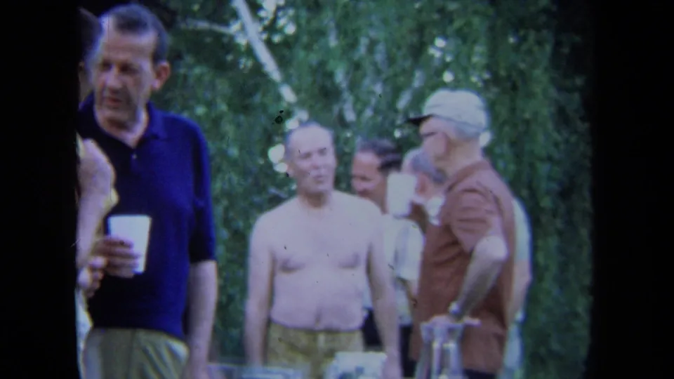 1971 California frame showing men in casual summer clothing standing with cups in a leafy backyard or garden.