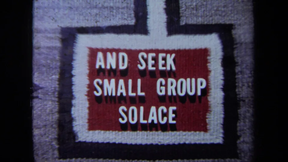 The camera moves closer to the woven sign, making AND SEEK SMALL GROUP SOLACE more prominent.
