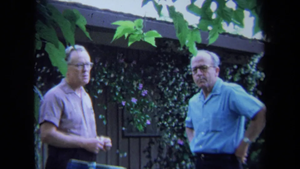 The two older men remain in the garden, standing before an ivy-covered wooden fence in 1971 California home-movie footage.