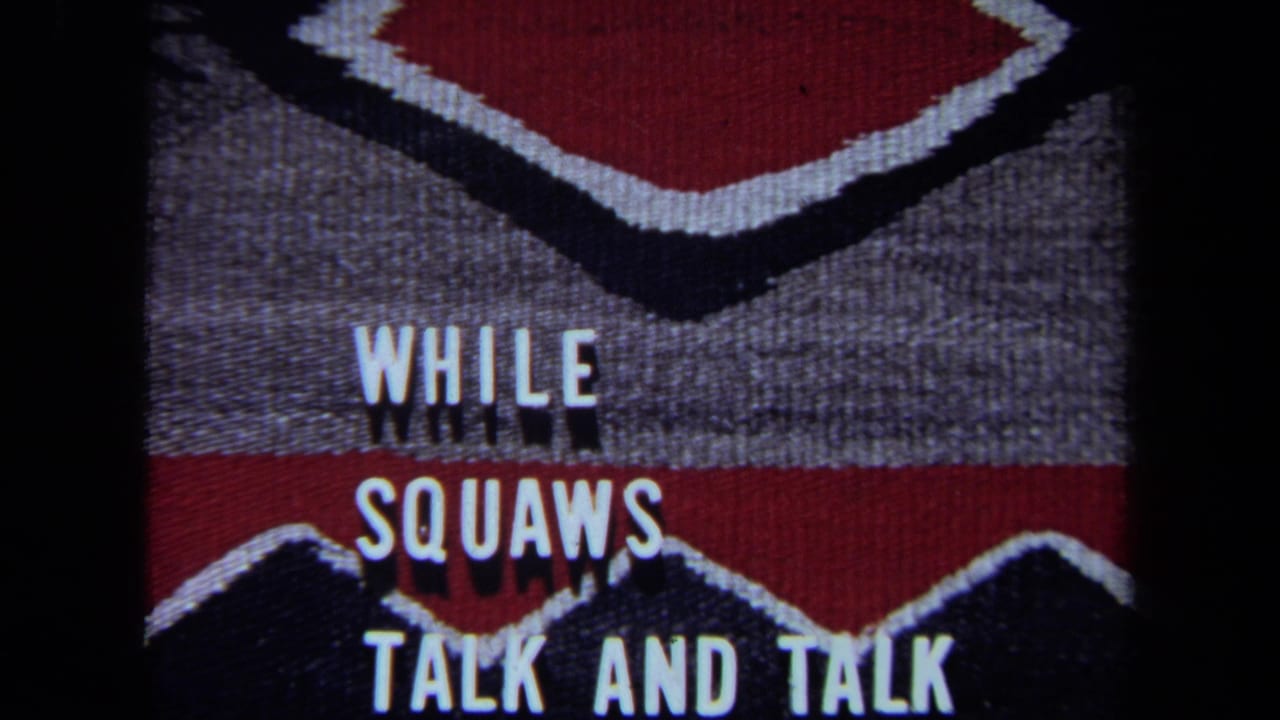 White block text reading “WHILE SQUAWS TALK AND TALK” over red, black, and gray geometric fabric.
