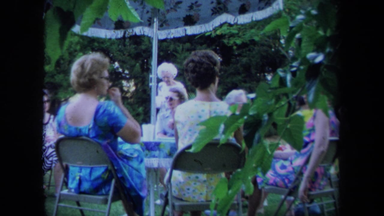 Older women sit in folding chairs near a garden table, with leaves crossing the foreground.