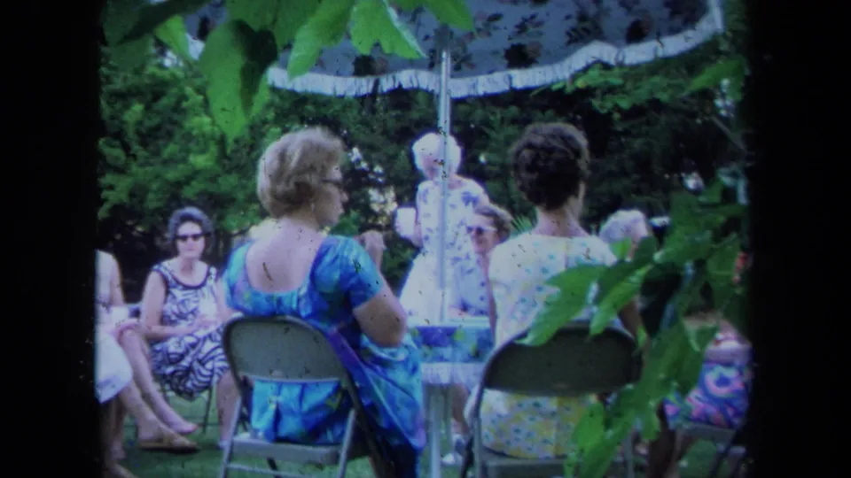 A 1971 California garden-party frame shows women seated in folding chairs, with a woman in blue prominent in the foreground.