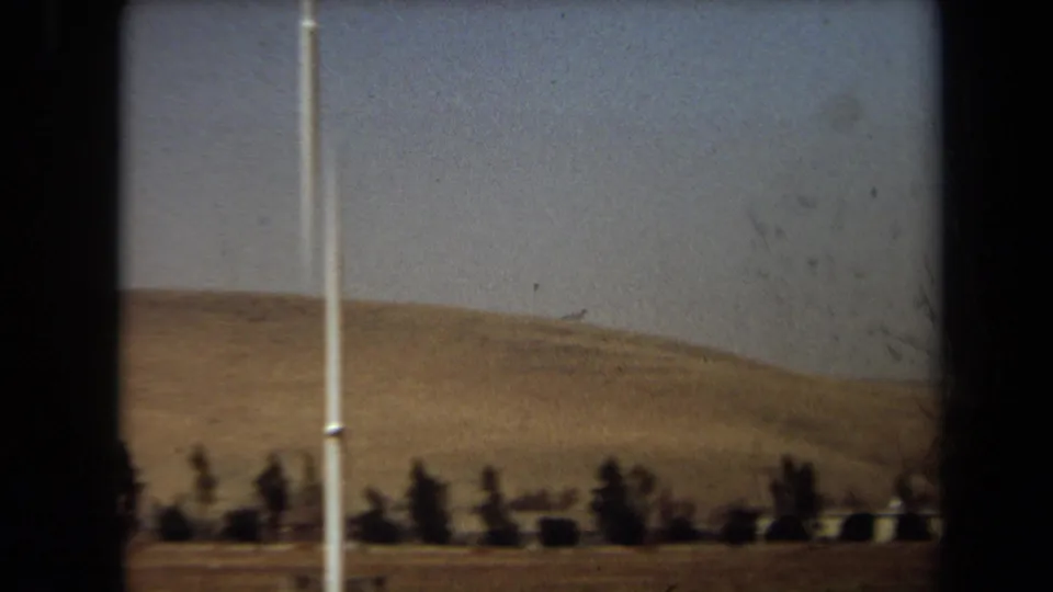 1971 Laguna Hills 8mm frame showing dry hills, hazy sky, and scattered roadside trees viewed from a moving position.
