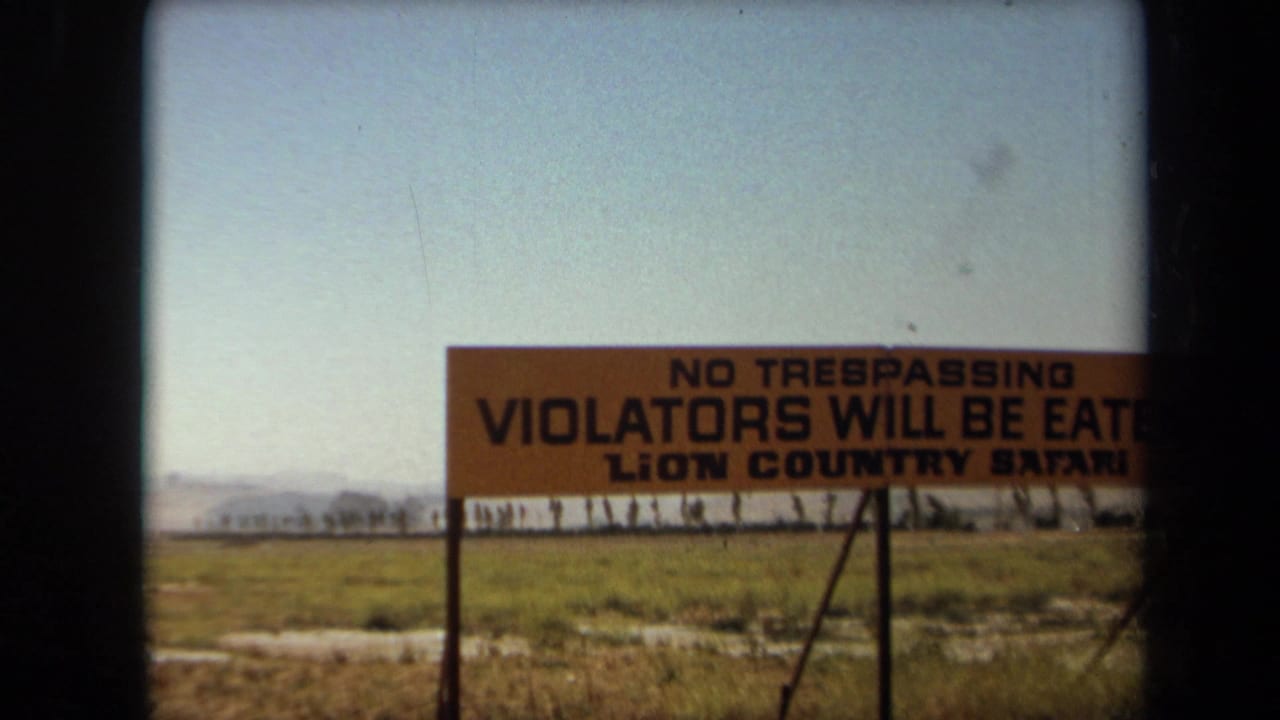 1971 Laguna Hills 8mm frame showing a Lion Country Safari warning sign in an open grassy field.
