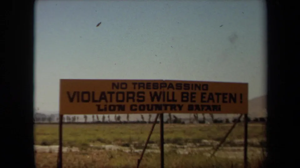 1971 Laguna Hills home-movie frame holding on the Lion Country Safari sign across a dry grassy foreground.