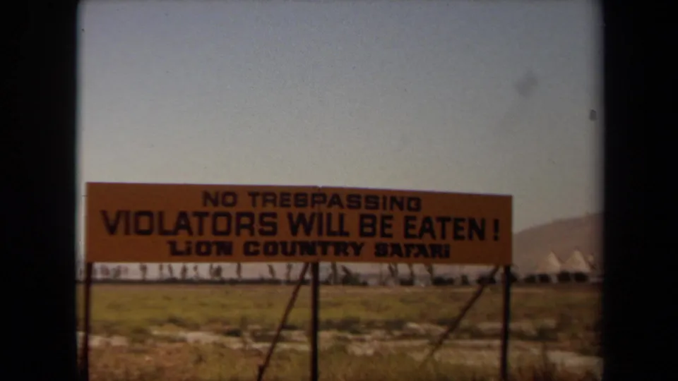 1971 Laguna Hills 8mm frame with the Lion Country Safari warning sign centered against grass, trees, and distant hills.