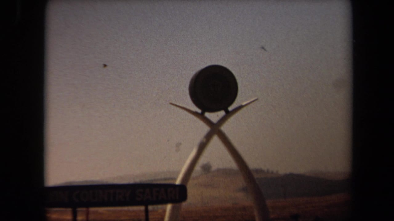 1971 Laguna Hills view of the Lion Country Safari entrance sign, partly framed by dark 8mm gate edges and a low horizon.