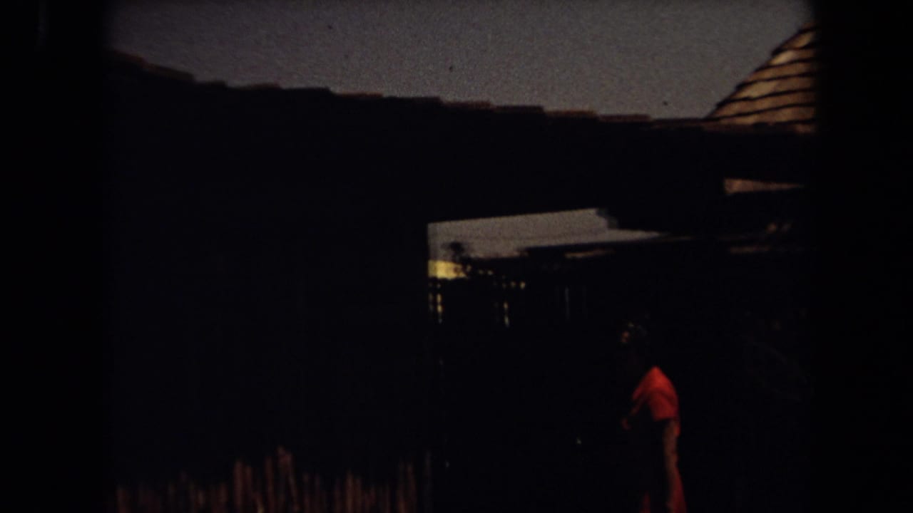 Dark exterior with a wooden roofline and a person in a red shirt walking near a structure.