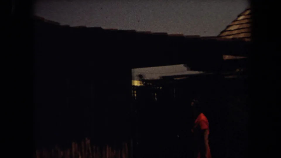 Dark 1971 Laguna Hills exterior with a shadowed wooden structure, roofline, and a person in a red shirt passing through the frame.