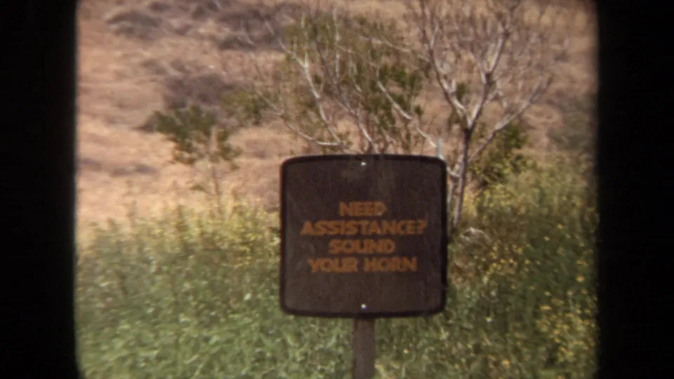 1971 Laguna Hills 8mm frame showing a roadside sign instructing visitors to sound the horn if assistance is needed.
