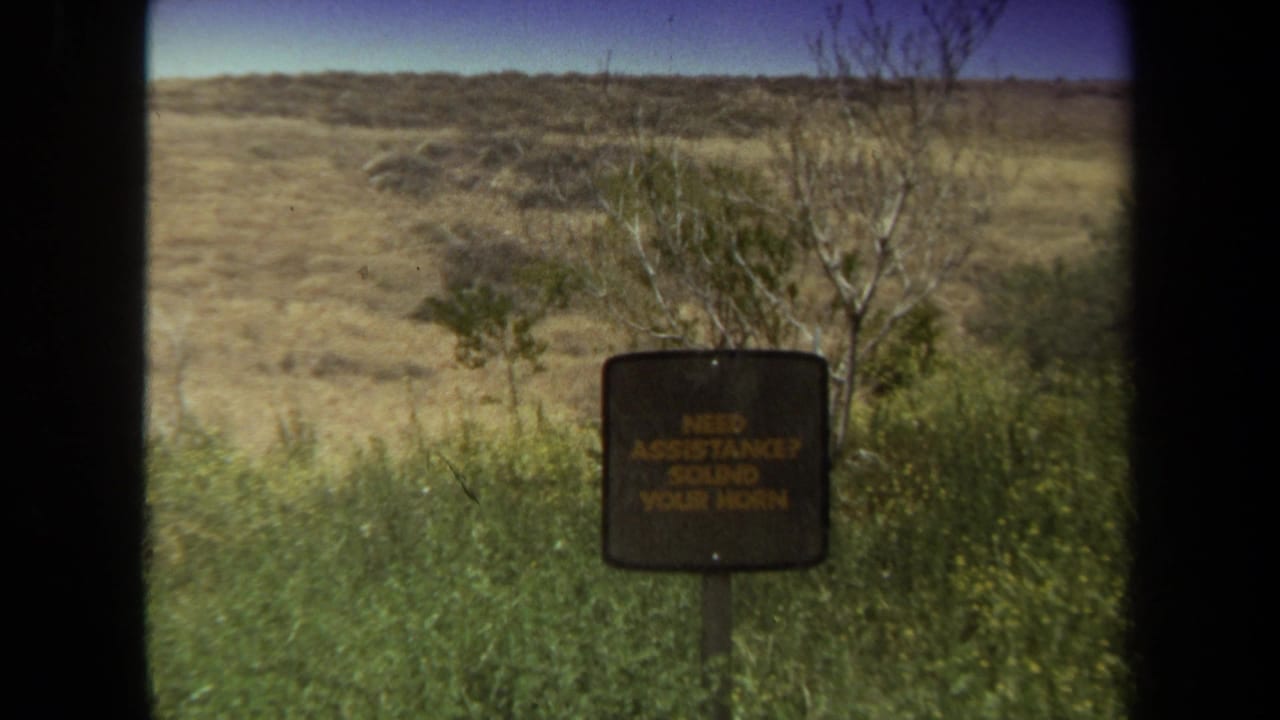 1971 Laguna Hills safari park view from a vehicle, with a small assistance sign, brush, open ground, and dark window edges.