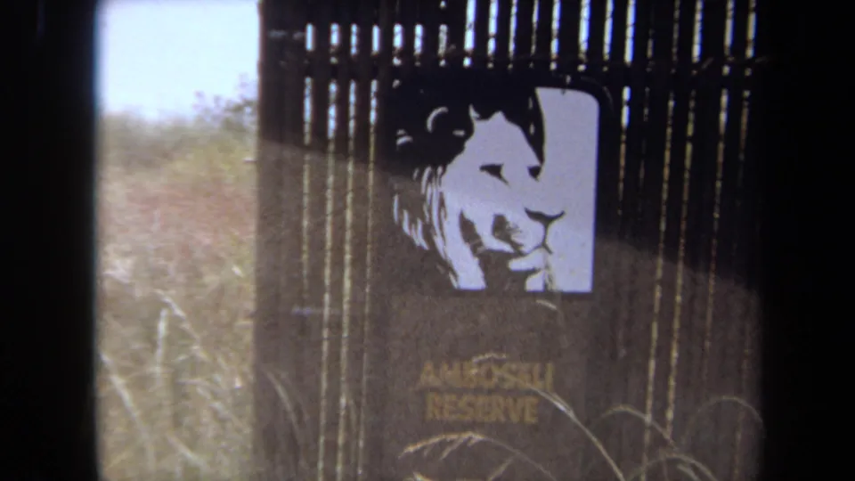 1971 Laguna Hills frame showing an Amboseli Reserve sign with a stylized lion face near fencing and grass, suggesting a themed animal display.
