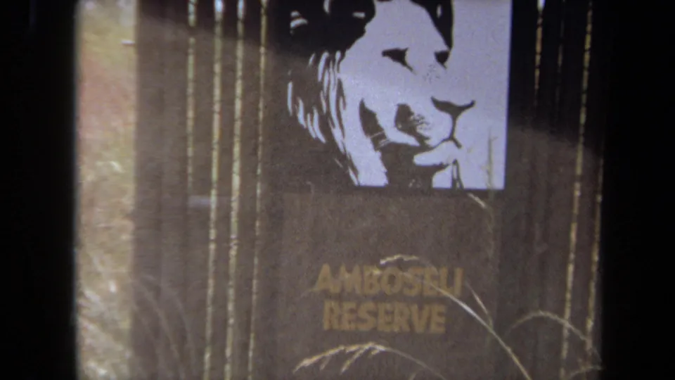 1971 8mm frame from Laguna Hills showing an Amboseli Reserve sign with a lion silhouette, partly obscured by dark film or framing edges.