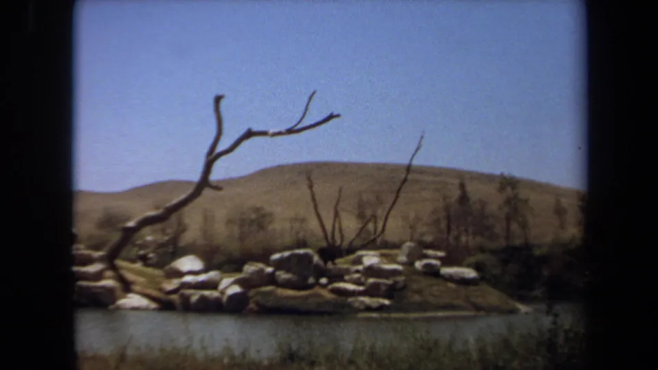 1971 8mm frame in Laguna Hills showing a rocky animal enclosure with bare branches, low brush, and dry hills in the background.
