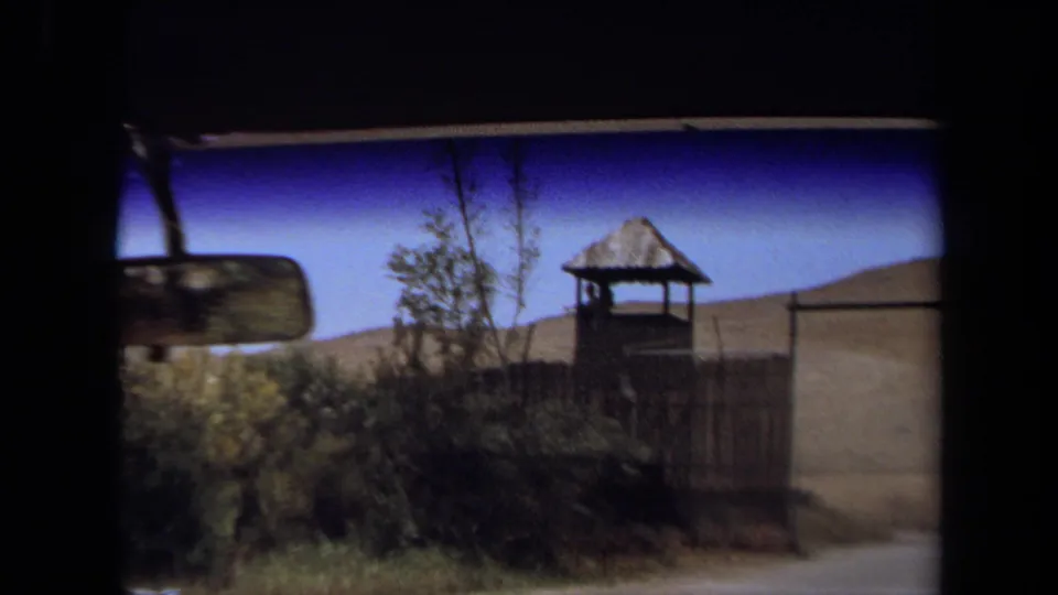 A vehicle-window view shows a rear-view mirror, fence, small tower-like structure, brush, and hills in 1971 Laguna Hills footage.