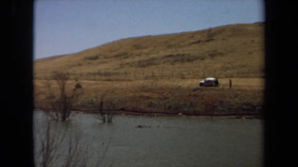 1971 Laguna Hills 8mm frame showing a parked car on a grassy hillside overlooking a pond and fenced shore.