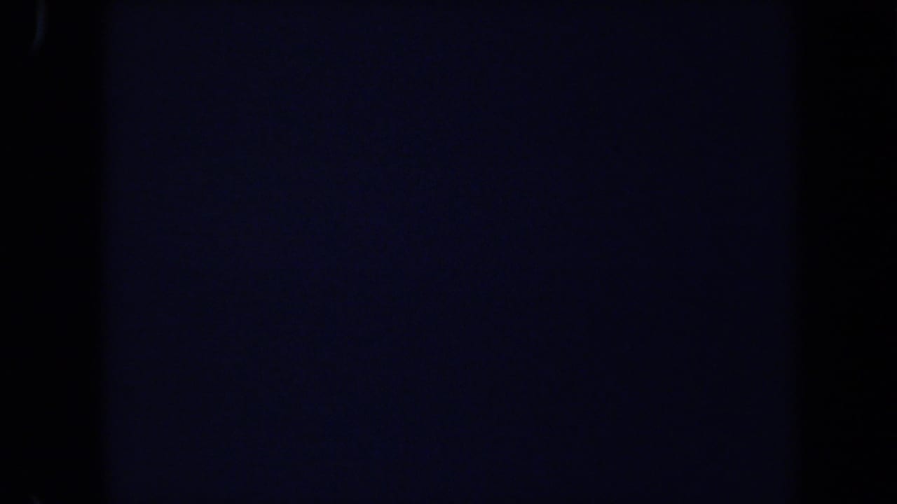 Underexposed 1971 8mm frame from the Laguna Hills zoo clip with only faint fence or structure detail visible.
