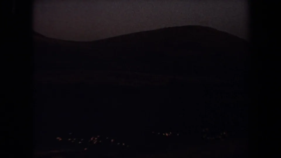 Dark, underexposed 1971 Laguna Hills frame showing a silhouetted hillside, dim waterline, and small bright birds near the lower edge.