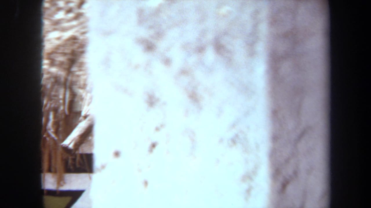 A 1971 8mm frame from Laguna Hills shows a partially obscured thatched structure with painted geometric wall detail.