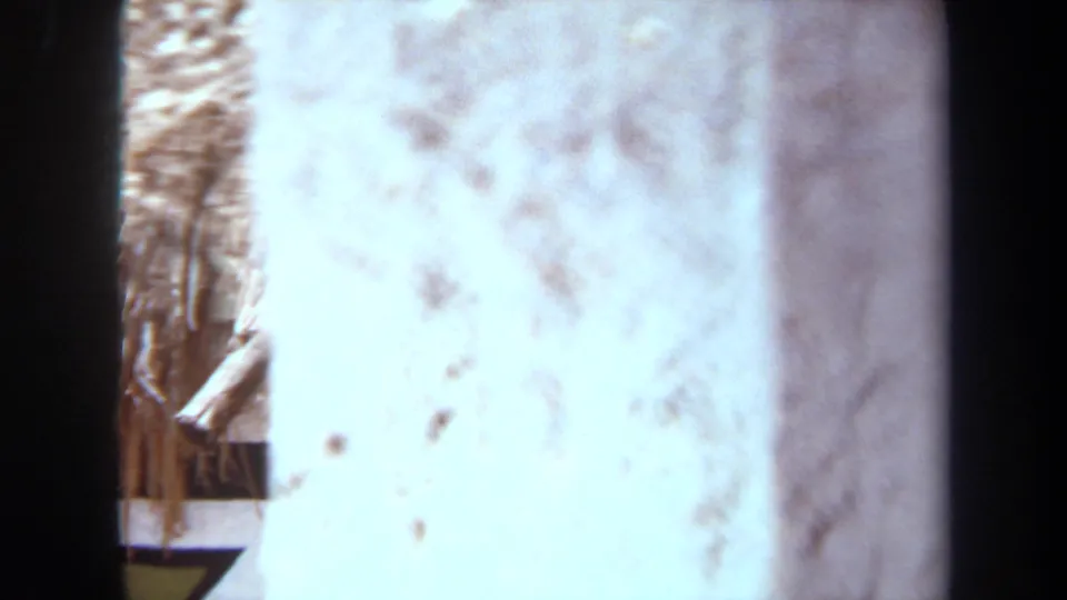 A 1971 8mm frame from Laguna Hills shows a partially obscured thatched structure with painted geometric wall detail.