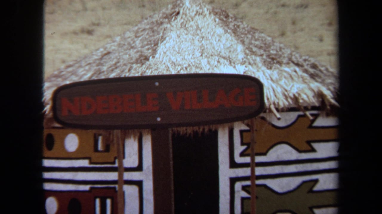 Thatched hut entrance with painted geometric walls and an Ndebele Village sign.