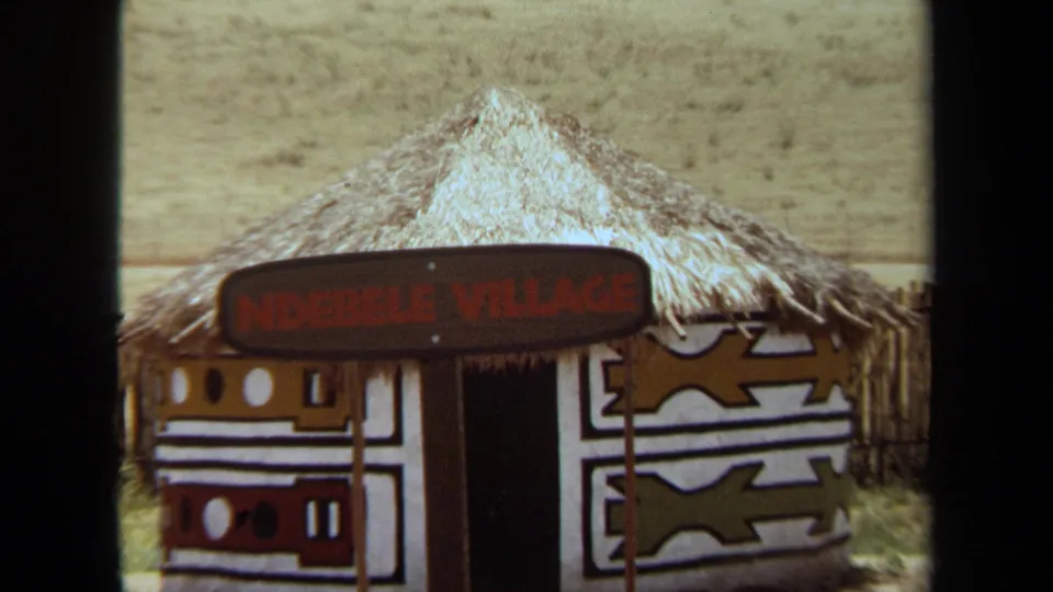 The 1971 home-movie view centers on a thatched Ndebele Village exhibit hut with bold geometric wall painting and a dark doorway.