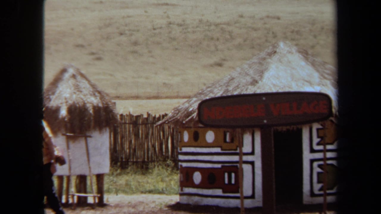Thatched hut exhibit with a sign reading Ndebele Village and dry open land behind it.