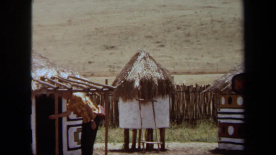 1971 Laguna Hills frame with a man walking through the recreated Ndebele Village exhibit beside thatched roofs and painted walls.