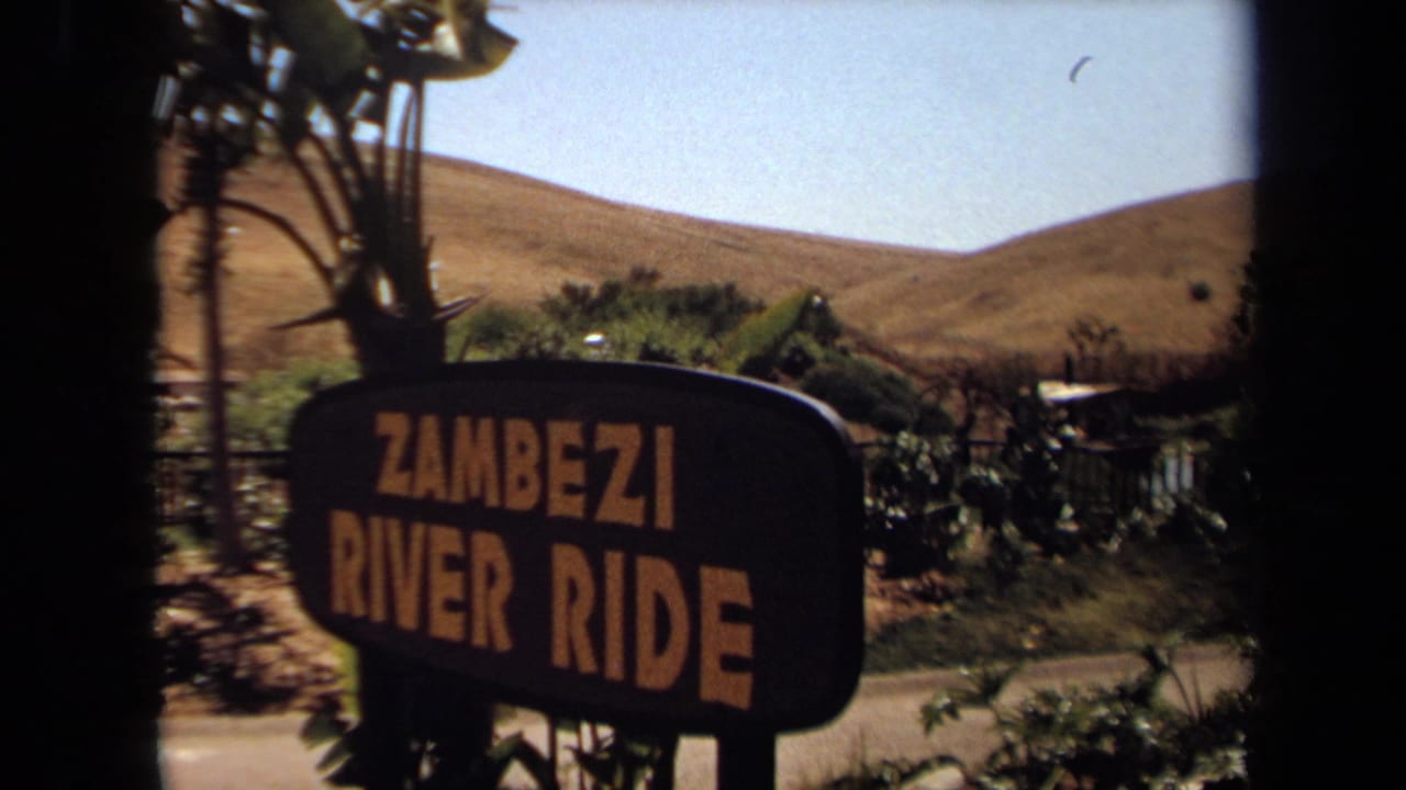 1971 8mm frame showing a Zambezi River Ride sign at a California attraction, with dry hills and foliage behind it.