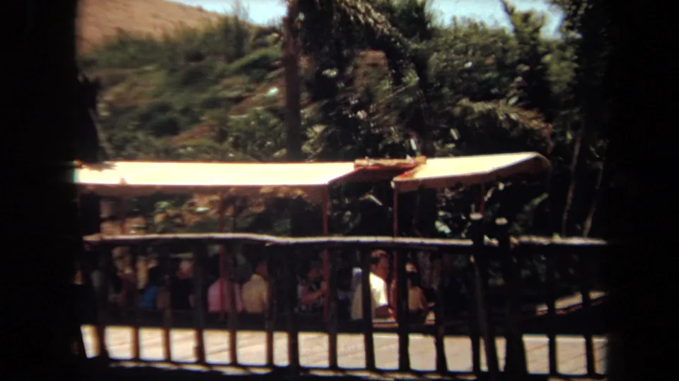 1971 Laguna Hills 8mm frame showing a canopy-covered riverboat with visible passengers, rail fencing, trees, and landscaped foliage.