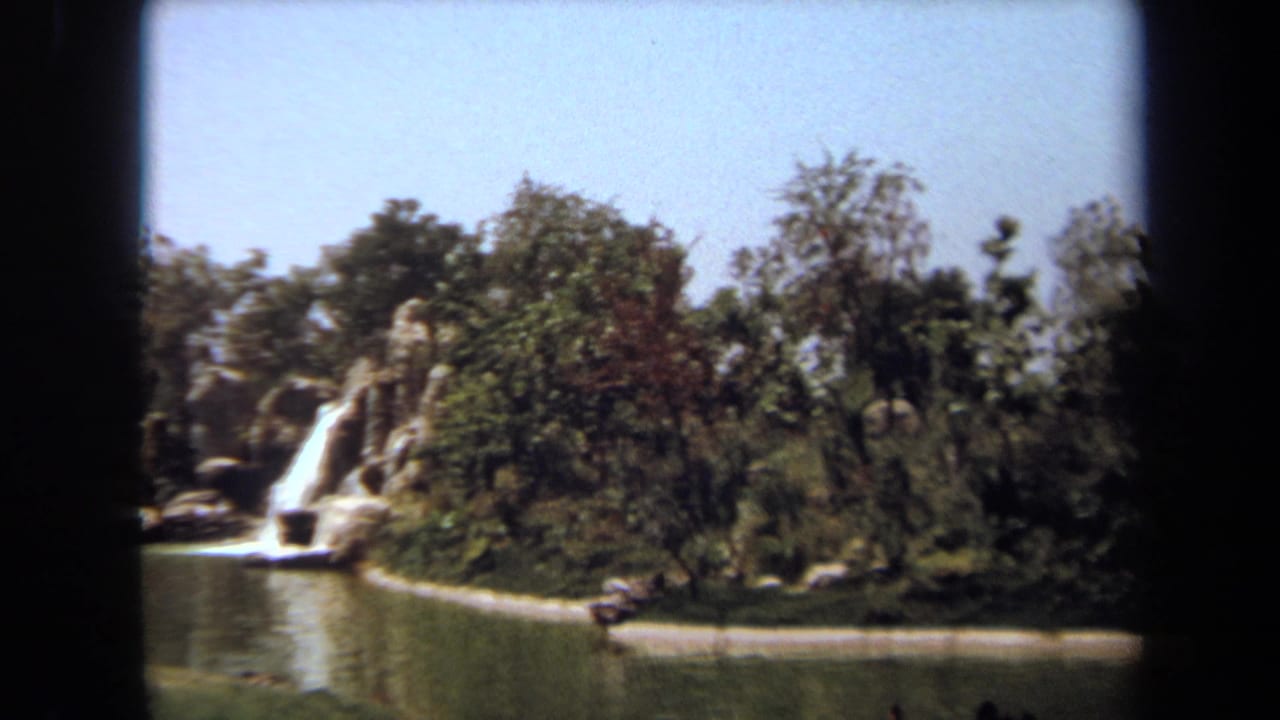1971 Laguna Hills 8mm frame showing ducks on a pond beside trees, rock edging, and a small artificial waterfall.