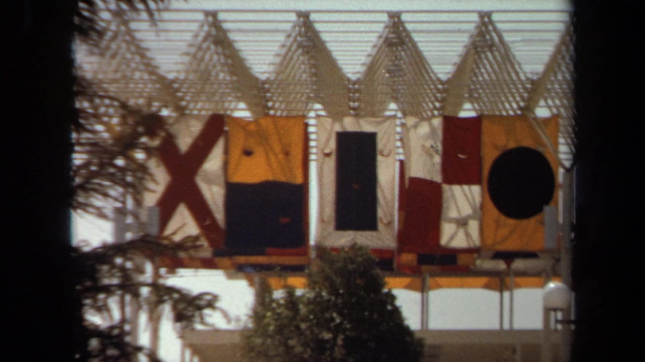 1971 Laguna Hills 8mm frame showing a close exterior view of a fort-like structure with large signal-style flags and trees in front.