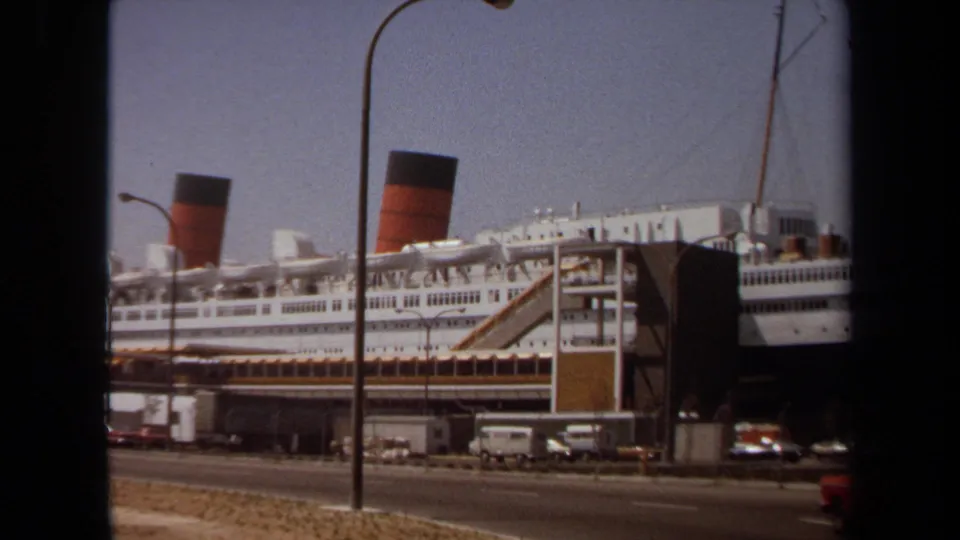 The final 1971 8mm frame holds on the docked liner, with a red car at the road edge and port structures in front of the ship.