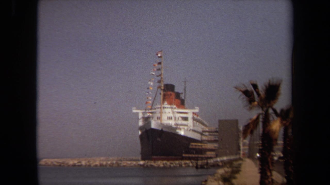 1971 Long Beach home-movie frame showing a large black-and-white ocean liner docked under a hazy sky.
