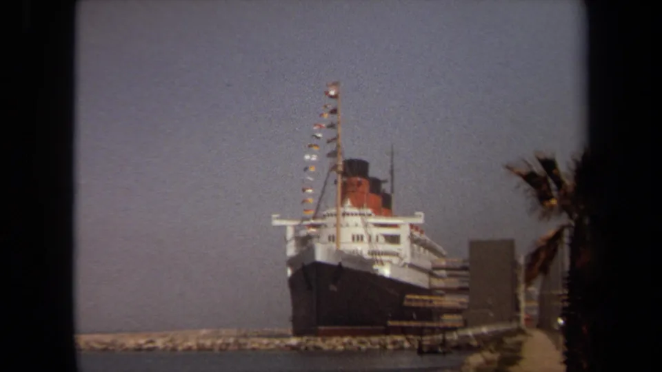 Long Beach 1971 8mm view of a docked ocean liner, seen from a shore path or waterfront overlook.