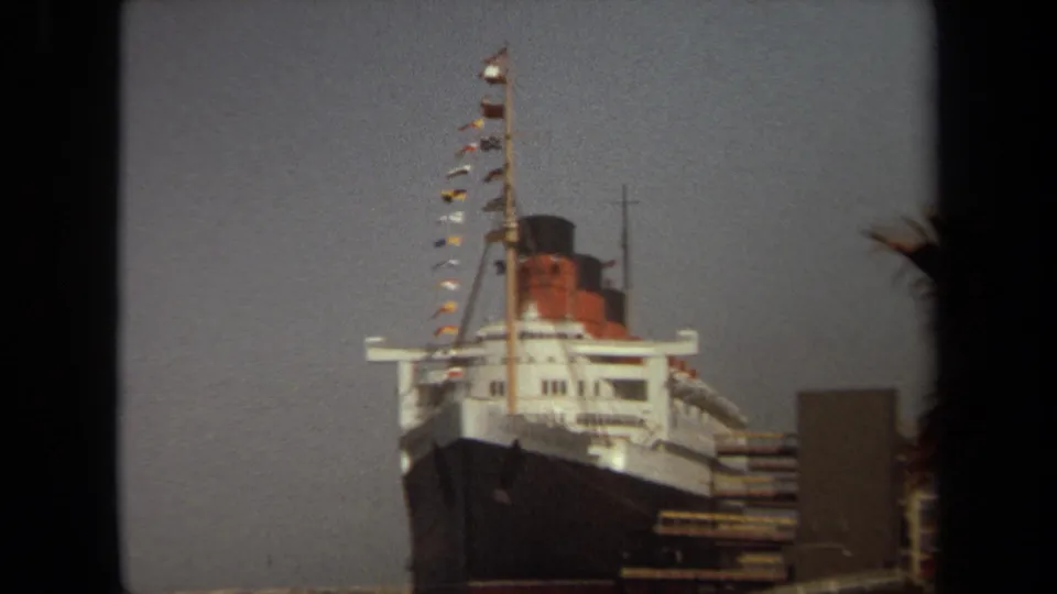 1971 Long Beach 8mm frame of a large ocean liner docked at port, with palm fronds just outside the main view.