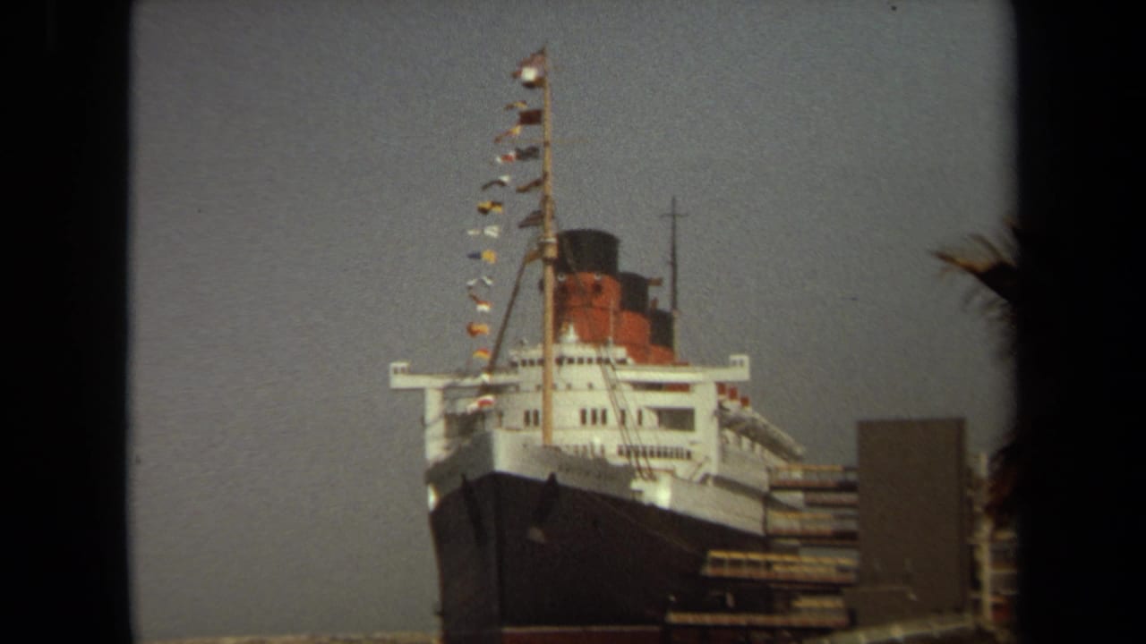 Docked Queen Mary bow and signal flags seen through a dark vertical foreground edge.