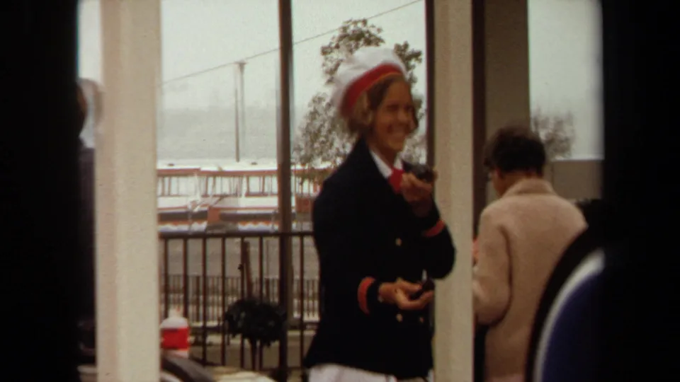 Uniformed guide or stewardess-style worker smiles inside a Long Beach terminal, with passengers, railings, and harbor windows behind her.
