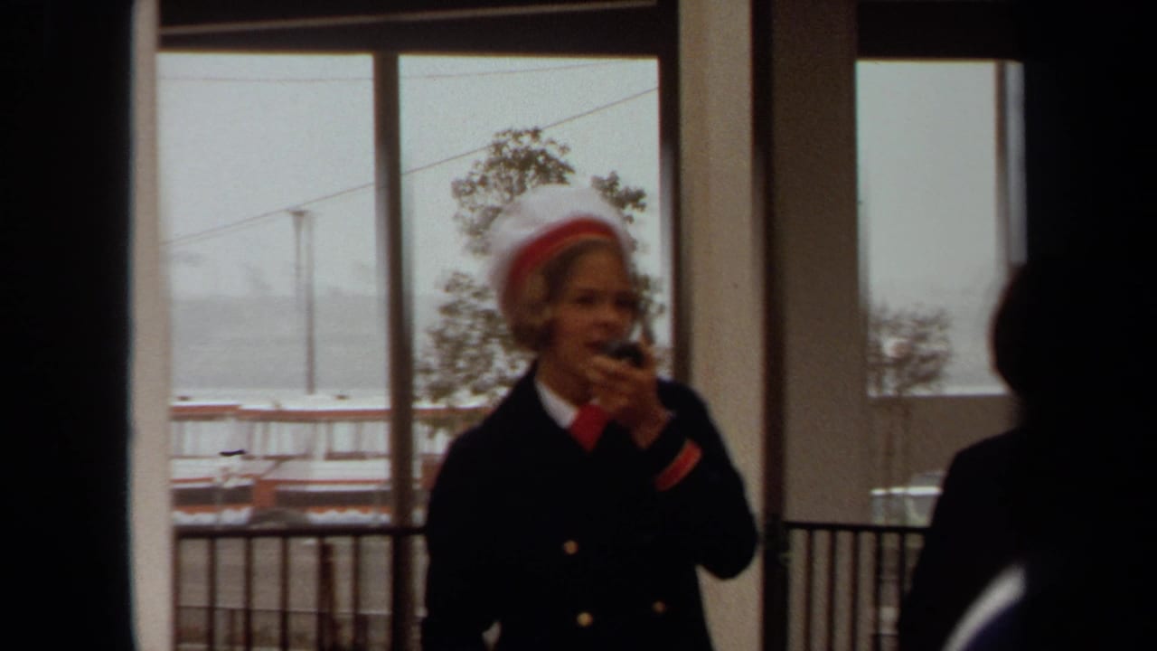 At a Long Beach cruise ship dock in 1971, a uniformed woman appears to make an announcement beside large windows overlooking the port.