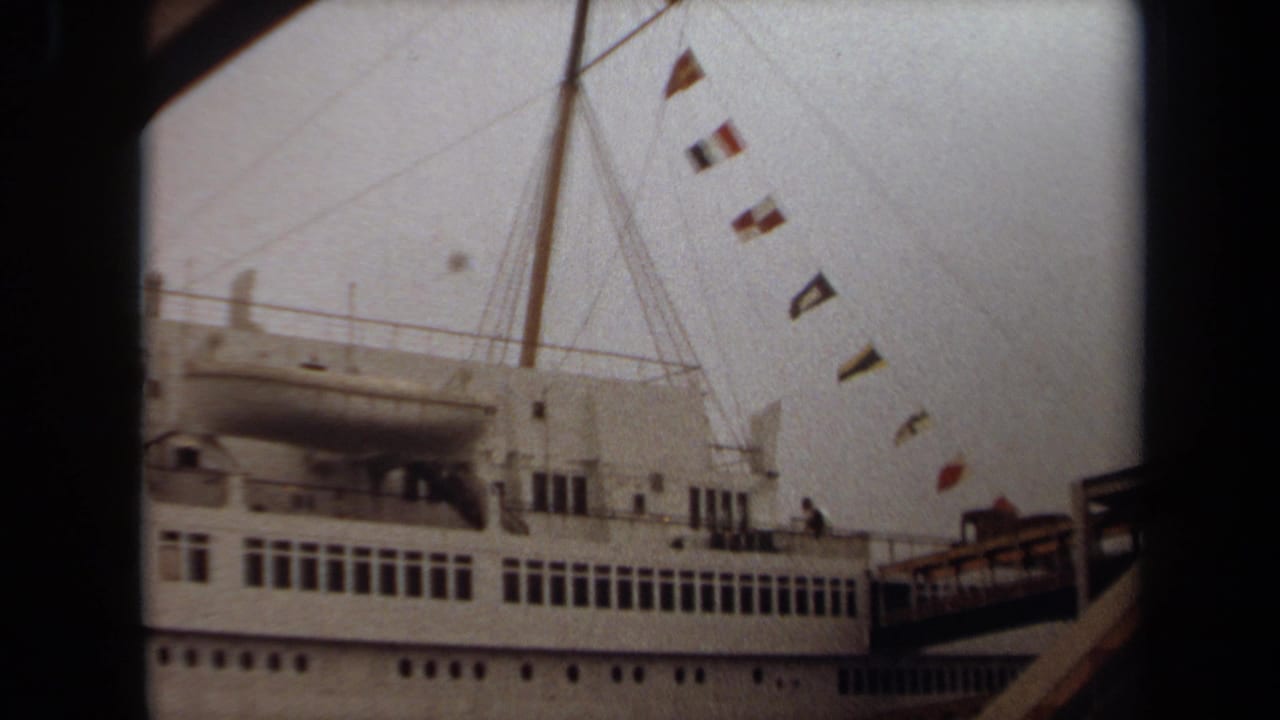 White cruise ship side with mast rigging, signal flags, and gangway at the pier.