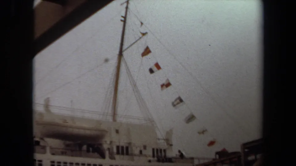1971 Long Beach frame with the ship mast, rigging, colorful signal flags, upper deck windows, and gangway edge visible.