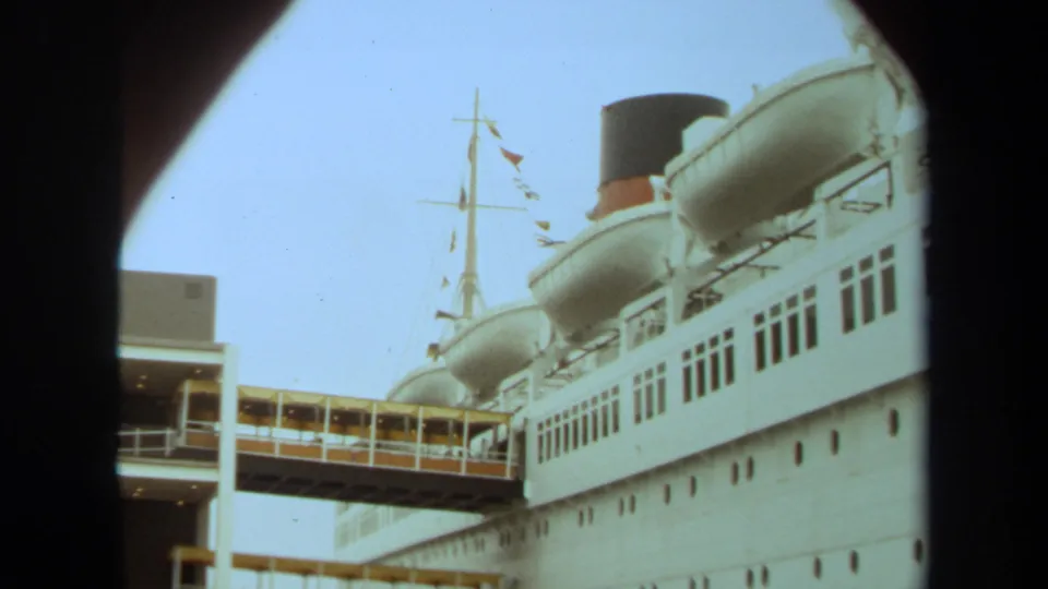 1971 Long Beach frame showing a white cruise ship beside the pier, with lifeboats, funnel, rows of windows, mast flags, and gangway.