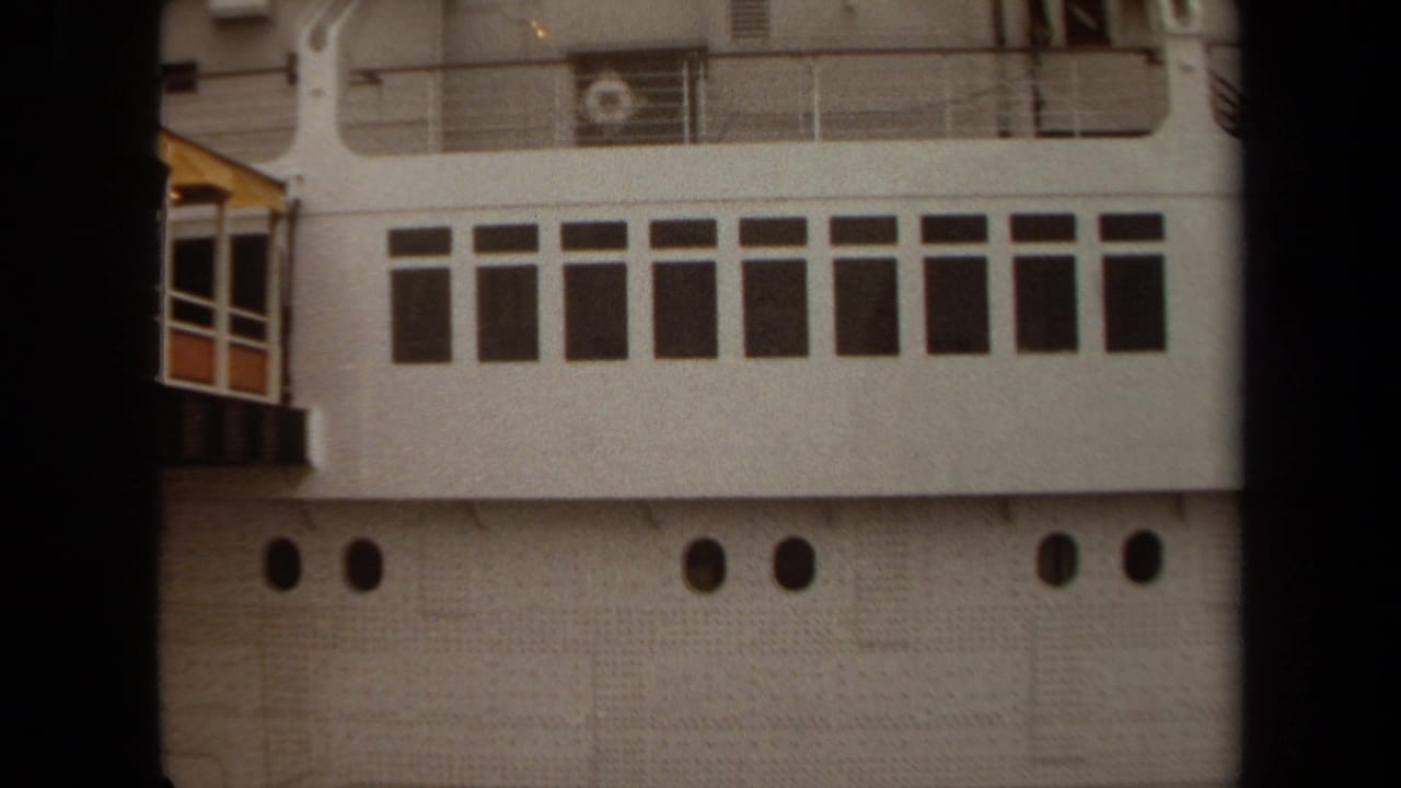 1971 Long Beach home-movie frame showing a docked passenger ship with rectangular windows, portholes, railings, and a yellow gangway.