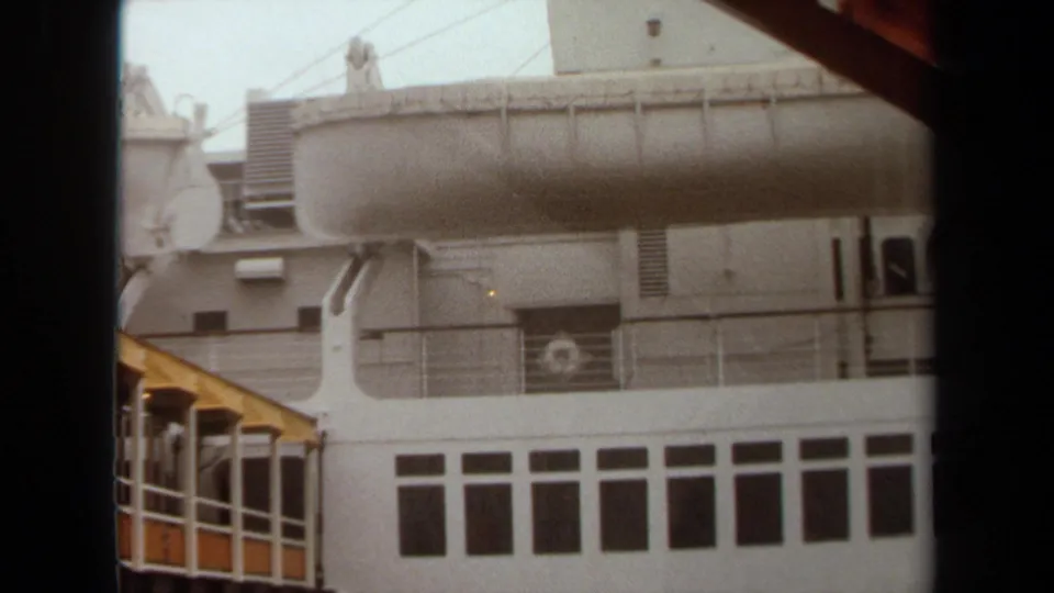 1971 Long Beach 8mm frame with the ship's lifeboat, railings, window rows, portholes, and yellow gangway partially visible.